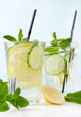 Sarı limonlu 2 bardak limonata, bir dilim taze salatalık ve mavi zemin üzerinde tüpler olan nane şekeri.