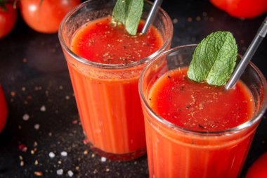 2 bardak nane ve baharatlı domates suyu, tuz, biber ve tüpler, siyah arka planda taze kırmızı domates, üst manzara, kapat.