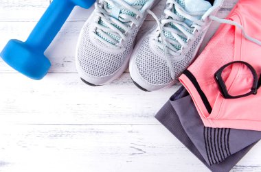 Gri spor ayakkabı, pembe bluz, spor giysi, 1 mavi halter, beyaz ahşap arka plan manzaralı bilezik.