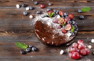 Taze böğürtlenli çikolatalı pasta, yaban mersinli pasta, üzüm, pudra şekeri ve tahta zemin üzerinde nane şekeri.