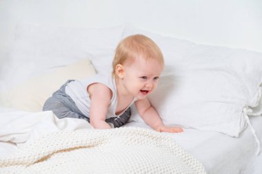 Gri pantolonlu beyaz bir kız yatakta ağlıyor, üzgün bebek.
