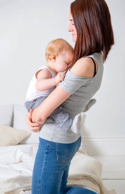 Beyaz, genç anne, parlak bir odada küçük kızını kollarında tutuyor, bebeğim.