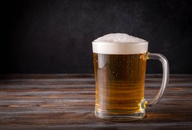 Koyu ahşap arka planda köpüklü 1 bardak açık arpa birası, alkollü içecek