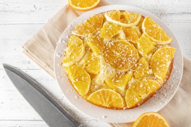 Taze portakallı yuvarlak turta, beyaz ahşap arka planda bir peçetenin üzerinde bıçak.