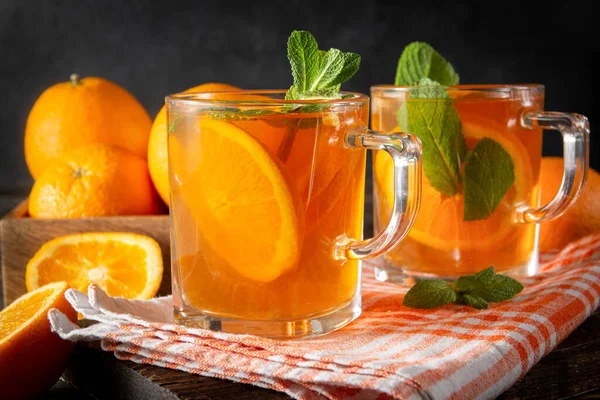 iced tea with orange and mint, fresh oranges on a towel on a dark wooden background