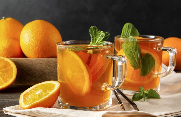 iced tea with orange and mint, fresh oranges on a towel on a dark wooden