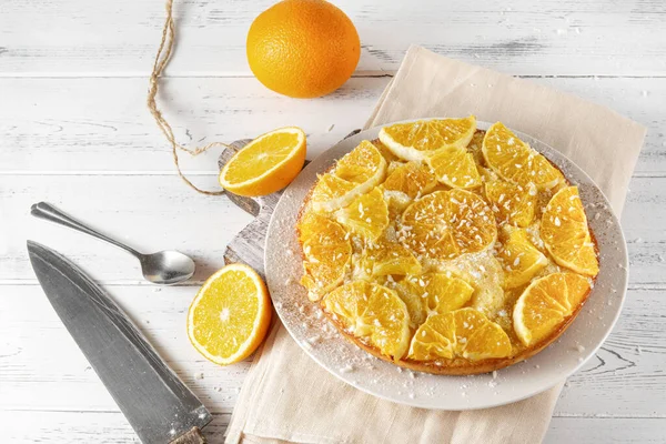 Taze portakallı yuvarlak turta, bir bıçak, beyaz ahşap arka planda bir kaşık.