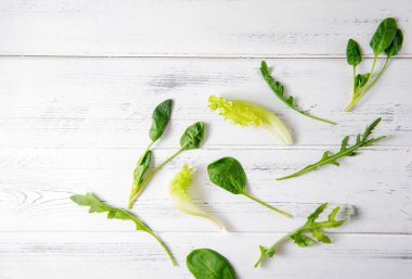 Beyaz ahşap zemin üzerinde yeşil taze ıspanak, marul ve roka filizleri.