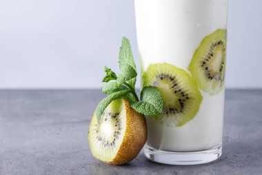 Bir bardak taze kivili yoğurt ve gri arka planda nane şekeri.