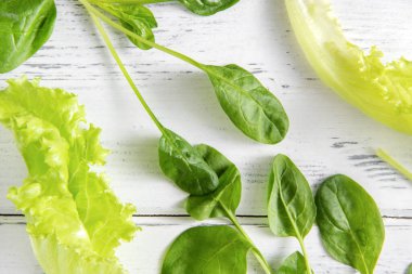 Taze yeşil marul, beyaz ahşap arka planda ıspanak yaprakları.