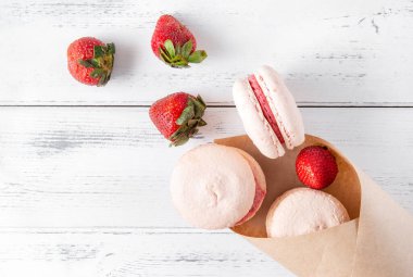 Beyaz ahşap arka plan manzaralı bir zarfın içinde çilekli bej Fransız kurabiyeleri.