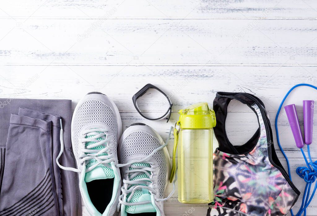 grey sneakers, leggings, top, jump rope, water bottle, sports bracelet, sportswear on a white wooden background