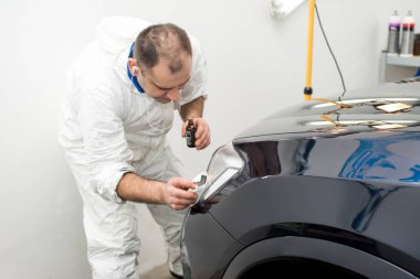 Oto yıkama makinesiyle araba cilalayan bir adam.