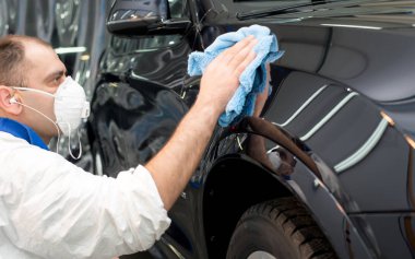 Oto yıkama makinesiyle araba cilalayan bir adam.