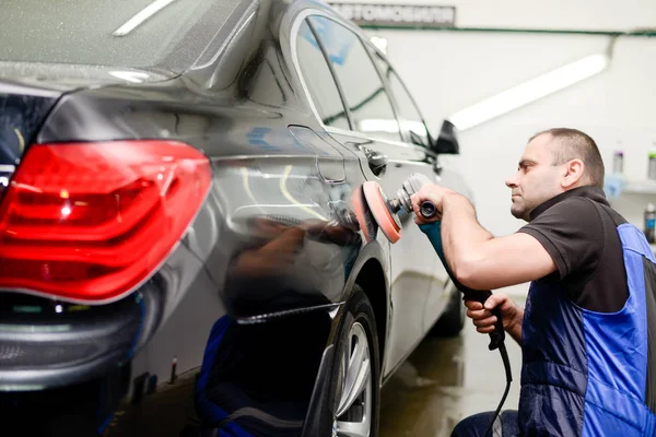 Oto yıkama makinesiyle araba cilalayan bir adam.