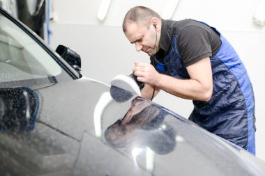 Oto yıkama makinesiyle araba cilalayan bir adam.