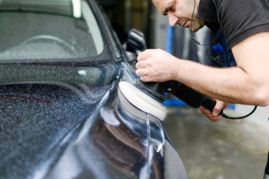 Oto yıkama makinesiyle araba cilalayan bir adam.