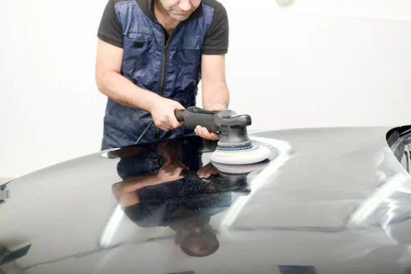 Oto yıkama makinesiyle araba cilalayan bir adam.