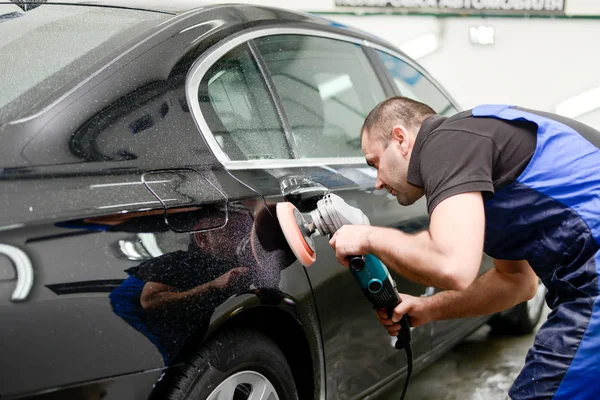 Oto yıkama makinesiyle araba cilalayan bir adam.
