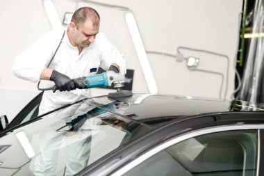 Oto yıkama makinesiyle araba cilalayan bir adam.