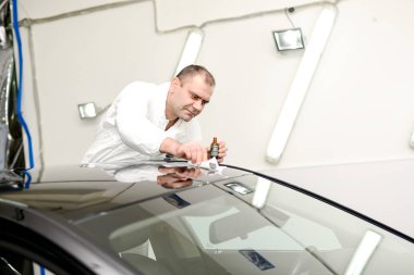 Oto yıkama makinesiyle araba cilalayan bir adam.