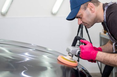 Bir adam siyah bir araba cilalama makinesi ile parlatır.