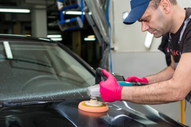 Bir adam siyah bir araba cilalama makinesi ile parlatır.