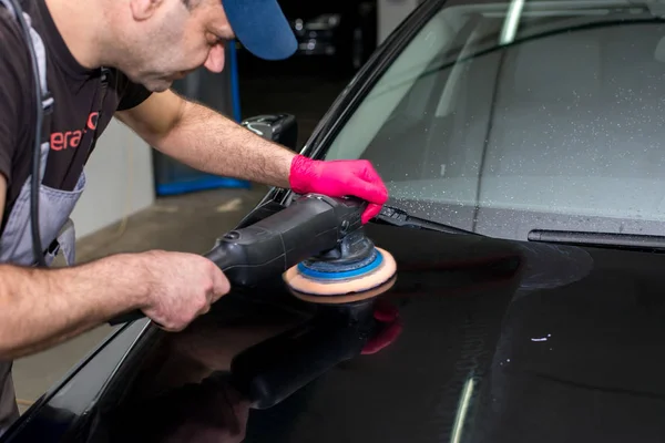 Bir adam siyah bir araba cilalama makinesi ile parlatır.