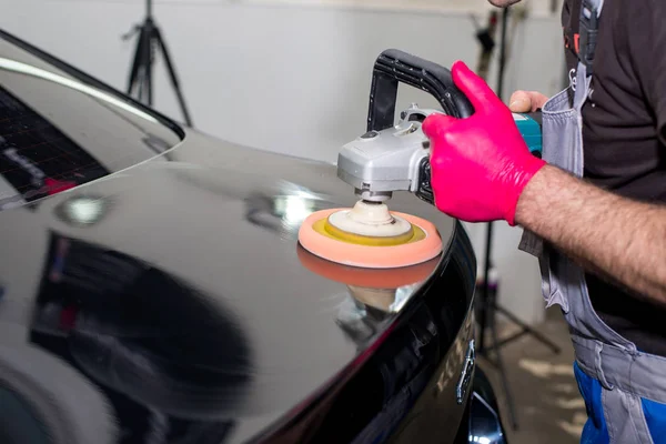 Bir adam siyah bir araba cilalama makinesi ile parlatır.