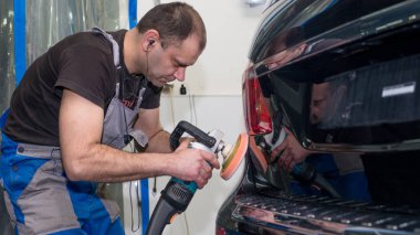 Bir adam siyah bir araba cilalama makinesi ile parlatır.