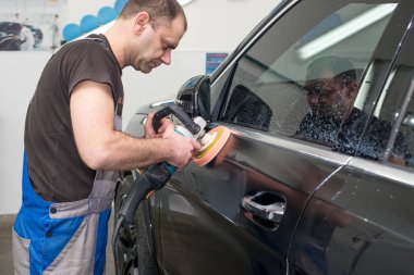 Bir adam siyah bir araba cilalama makinesi ile parlatır.