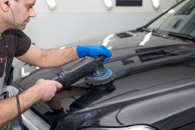 Bir adam siyah bir araba cilalama makinesi ile parlatır.