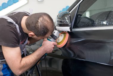 Bir adam siyah bir araba cilalama makinesi ile parlatır.