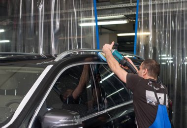 Bir adam siyah bir araba cilalama makinesi ile parlatır.