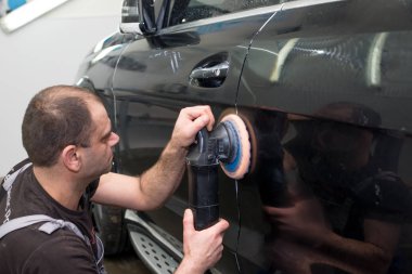 Bir adam siyah bir araba cilalama makinesi ile parlatır.