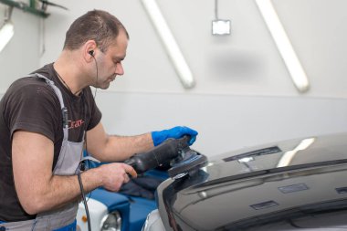 Bir adam siyah bir araba cilalama makinesi ile parlatır.