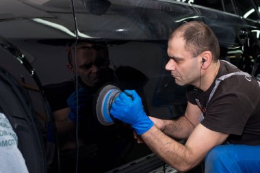 Bir adam siyah bir araba cilalama makinesi ile parlatır.