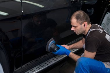 Bir adam siyah bir araba cilalama makinesi ile parlatır.