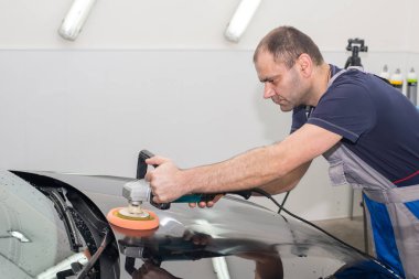 Bir adam siyah bir araba cilalama makinesi ile parlatır.