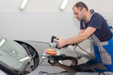 A man polishes a black car with a polishing machine clipart