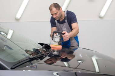 Bir adam siyah bir araba cilalama makinesi ile parlatır.