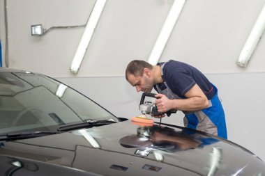 Bir adam siyah bir araba cilalama makinesi ile parlatır.