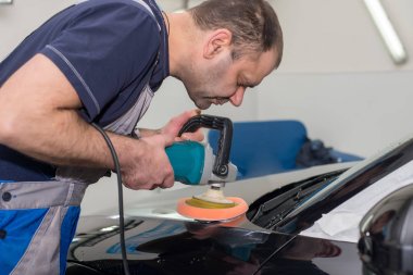 Bir adam siyah bir araba cilalama makinesi ile parlatır.