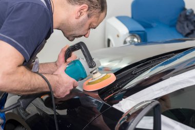 Bir adam siyah bir araba cilalama makinesi ile parlatır.