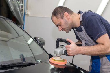 Bir adam siyah bir araba cilalama makinesi ile parlatır.
