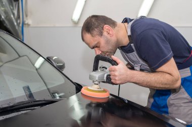 Bir adam siyah bir araba cilalama makinesi ile parlatır.