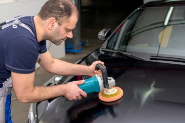 Bir adam siyah bir araba cilalama makinesi ile parlatır.