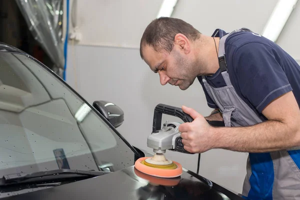 Bir adam siyah bir araba cilalama makinesi ile parlatır.