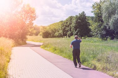 Bir adam parkta güneşli bir günde koşuyor