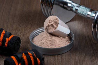 Ahşap arka plan üzerinde metal bir dumbbell ile ölçüm bir kova içinde peynir altı suyu proteini